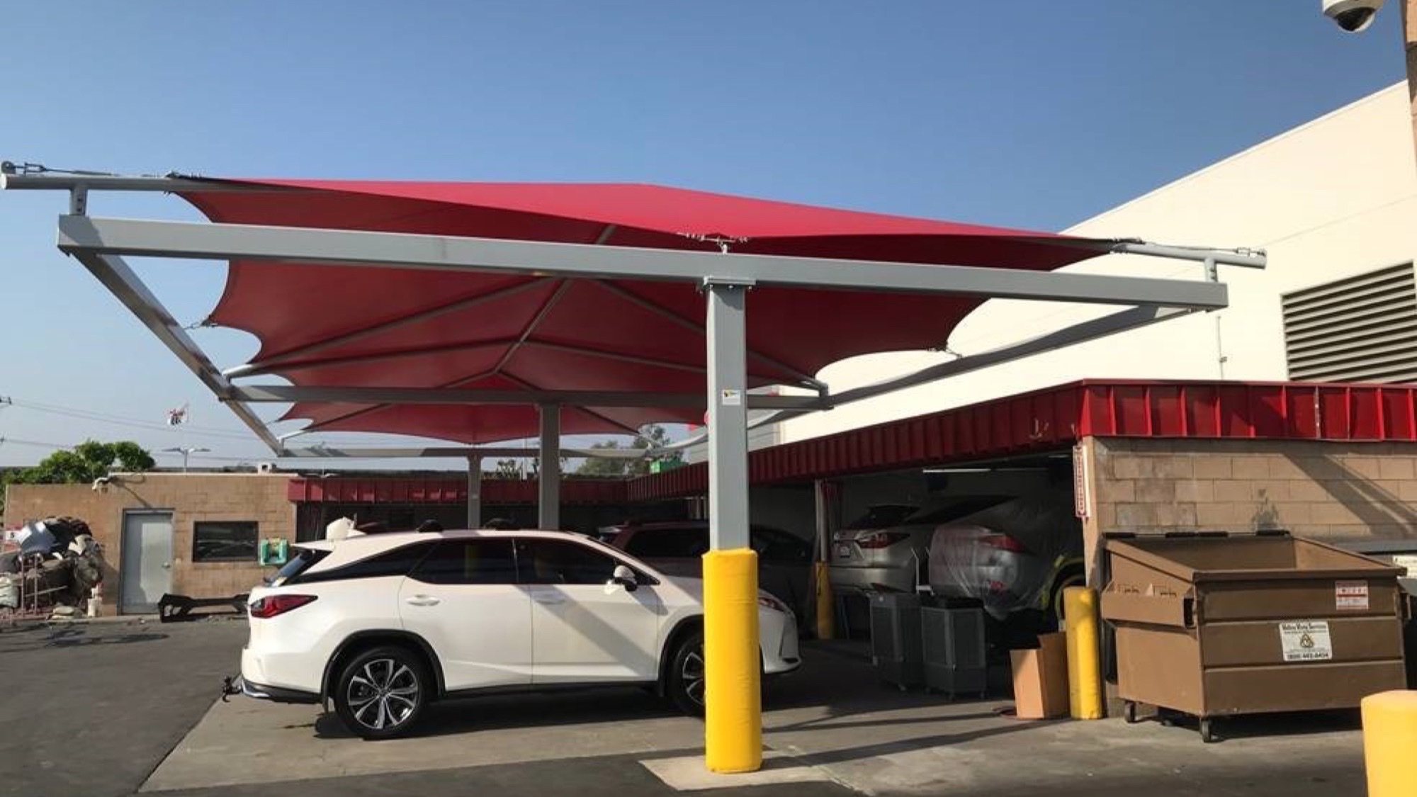 Red steel dealership service drive canopy shading vehicles at a dealership service bay
