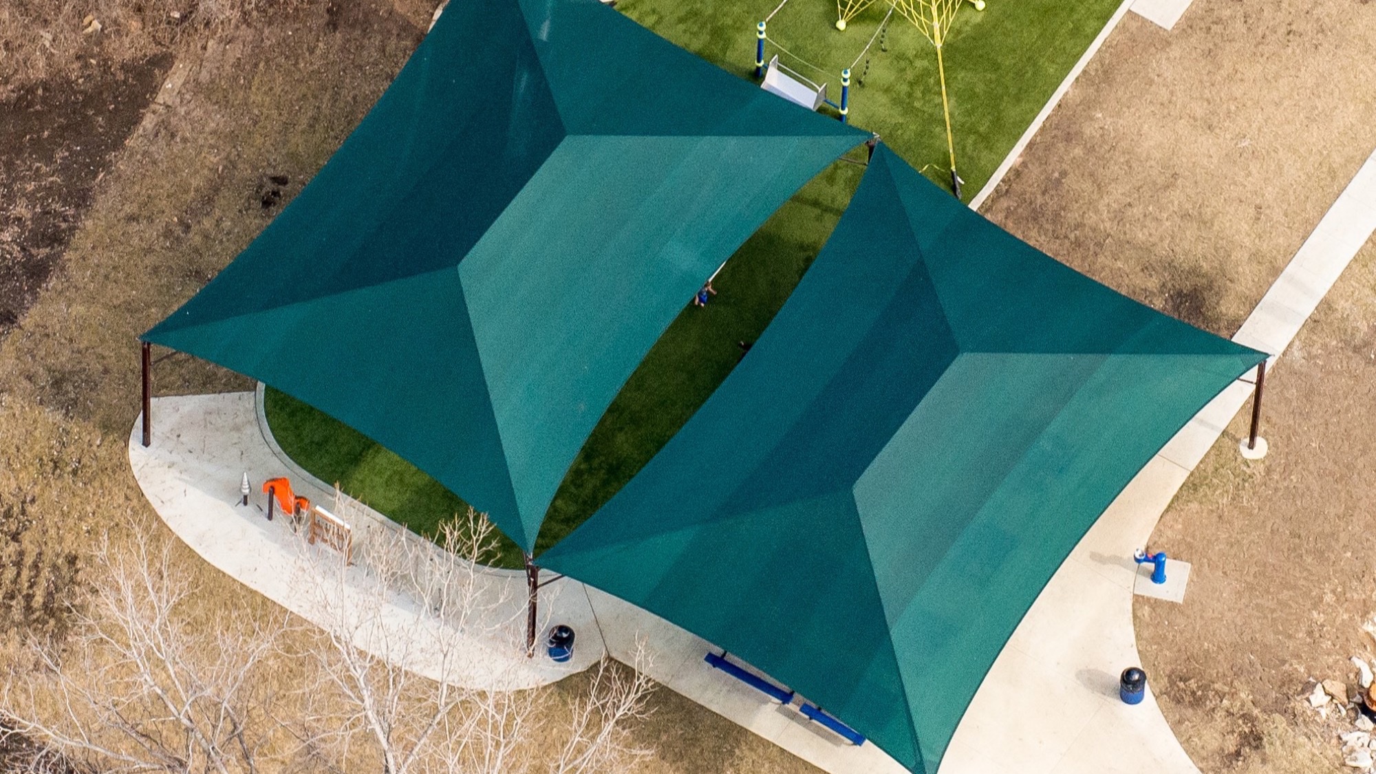Shade structures for community centers: double hip canopy over a courtyard seating area near a playground